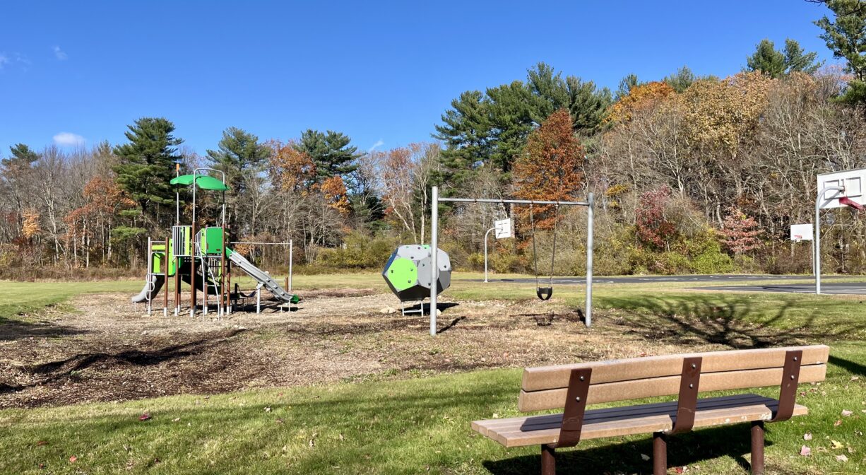 A photograph of a park with a playground and a bench.