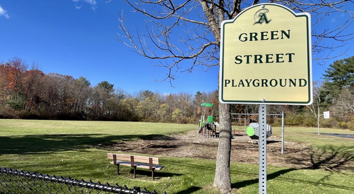 A photograph of a park with a property sign and a fence.