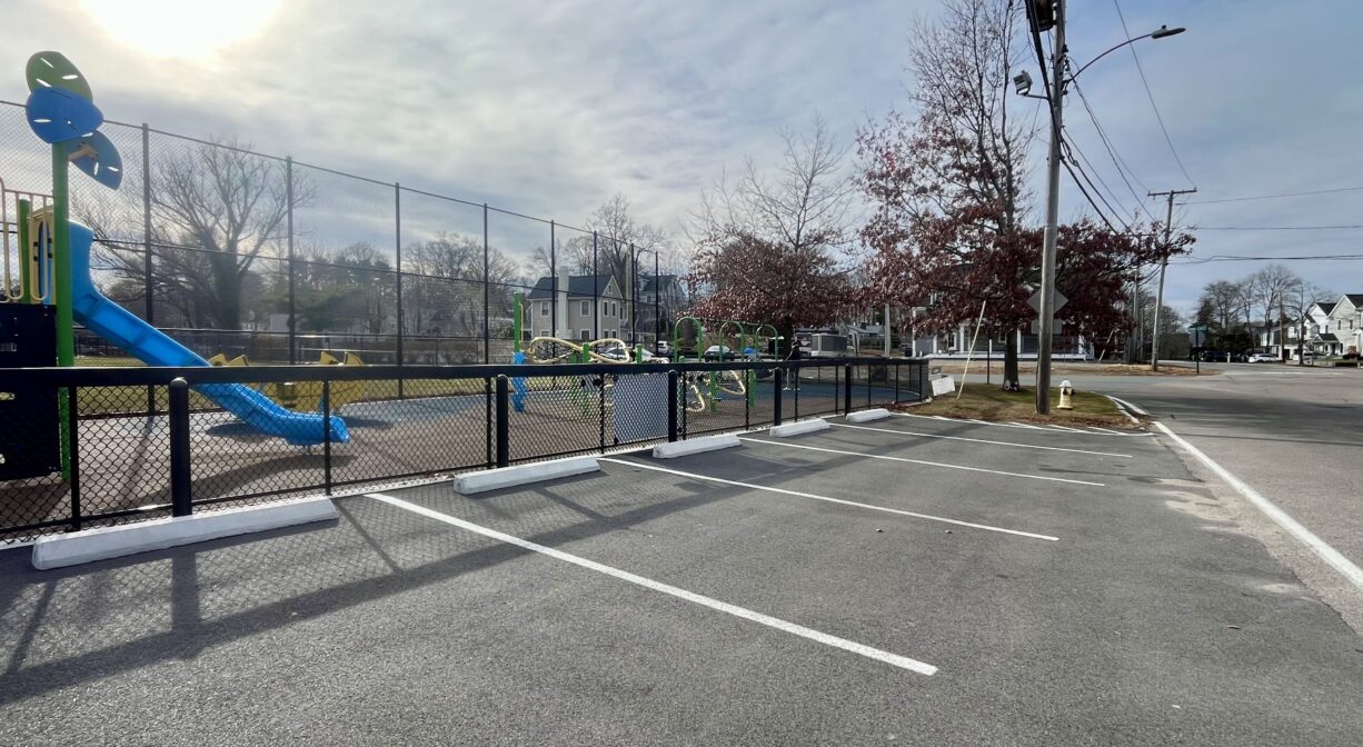 A photograph of a row of parking spaces beside a playground.