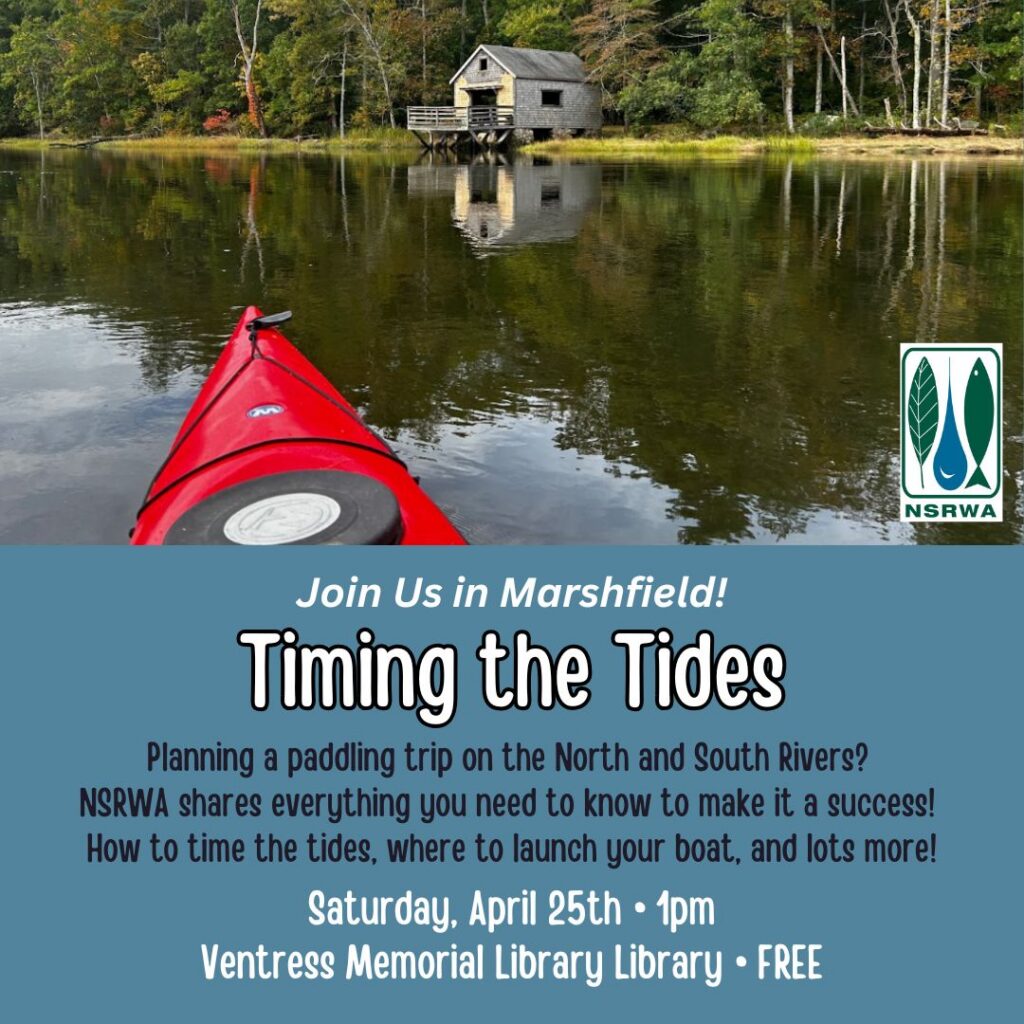 A photograph of the bow of a red kayak on a river with a boathouse in the distance.
